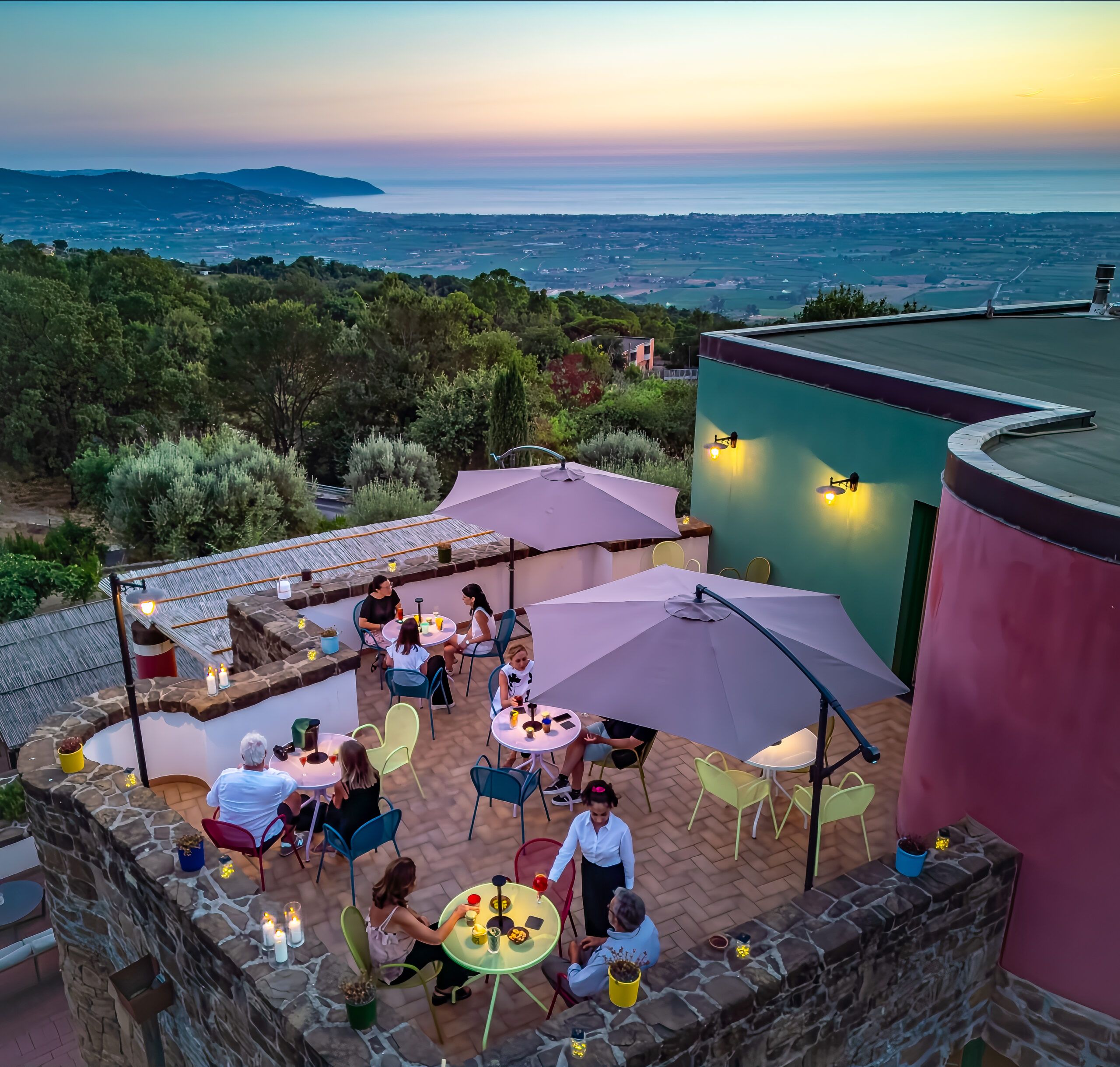 The upper terrace at Borgo La Pietraia at dusk — the plain of Paestum below, the Tyrrhenian Sea on the horizon, and the coloured architectural accents that echo the original pigments of the Greek temples. | Photo Courtesy of Borgo La Petraia