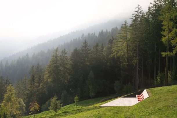 The terrace at Vigilius Mountain Resort, Vigiljoch — a wooden platform set into the alpine meadow at 1,500 metres, the larch forest rising into the morning mist. Slow Hospitality begins here, before the first choice of the day has been made. | Photo: Tobias Kaiser