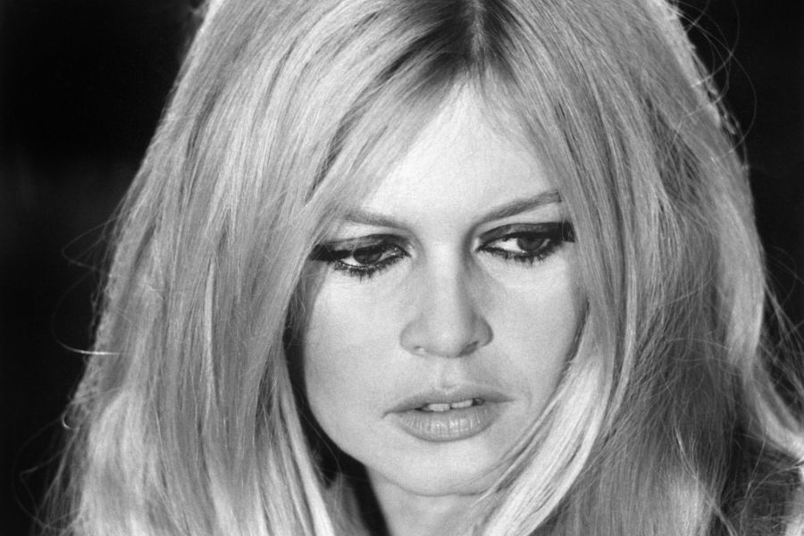 A black and white portrait of French icon Brigitte Bardot during a 1967 rehearsal at the ORTF studio in Paris. She is captured in a natural, candid moment that reflects the taste and eroticism of authenticity, wearing her signature hairstyle and an expressive look that defines her legacy of liberated fashion.