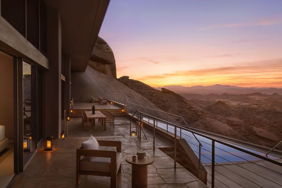 Minimalist luxury suite with a private infinity pool carved into massive sandstone desert rock formations at sunset in Saudi Arabia, illustrating deep immersion and the architecture of restoration.