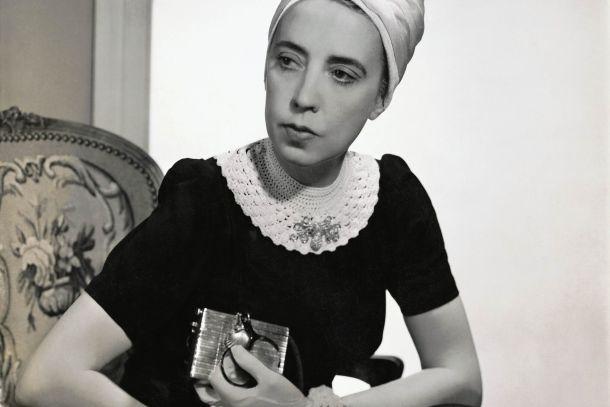 Elsa Schiaparelli wearing a black silk dress with crocheted collar of her own design and a white turban, seated in an upholstered chair holding a silver clutch. Vogue, 1940. Photograph by Fredrich Baker © Condé Nast via Getty Images.