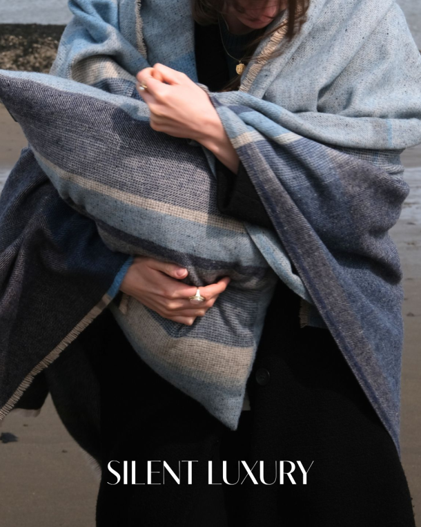 Person wrapped in a blue Coastland woven blanket on the beach