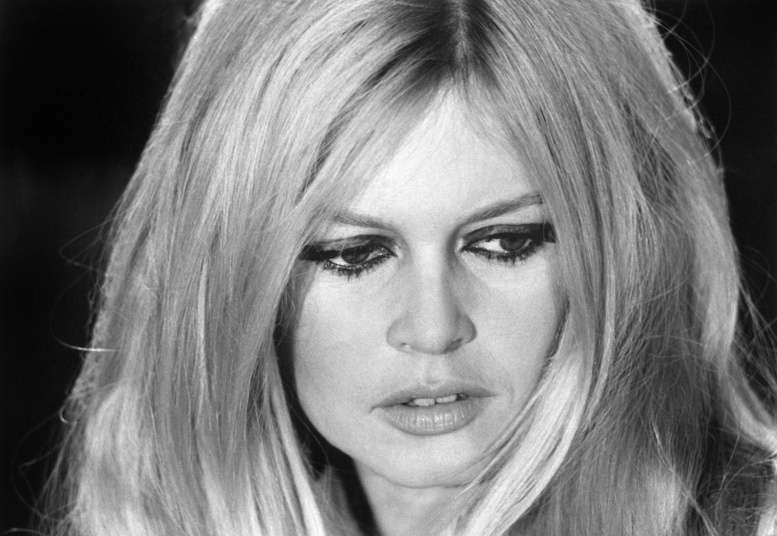 A black and white portrait of French icon Brigitte Bardot during a 1967 rehearsal at the ORTF studio in Paris. She is captured in a natural, candid moment that reflects the taste and eroticism of authenticity, wearing her signature hairstyle and an expressive look that defines her legacy of liberated fashion.