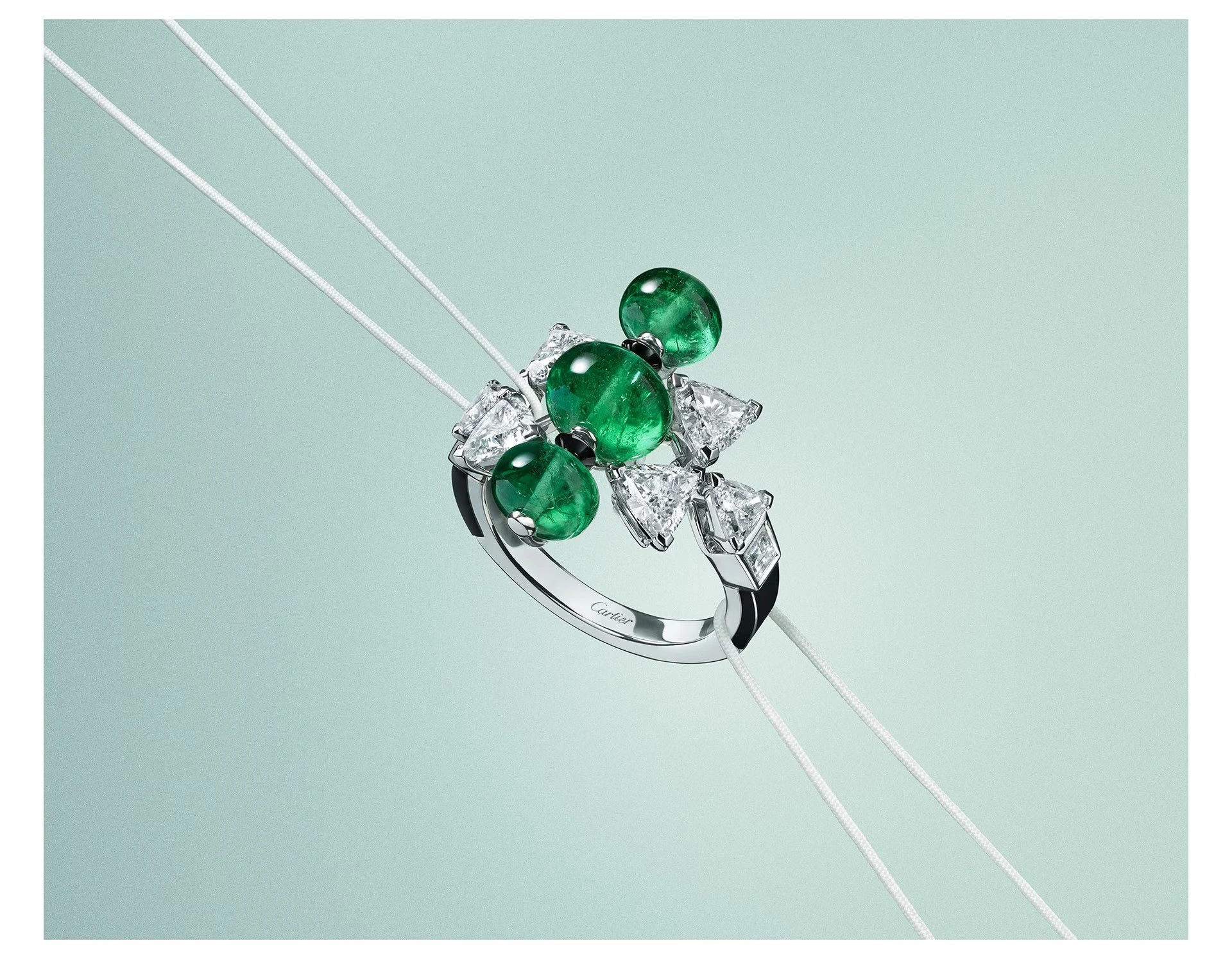 Cartier En Équilibre Summae ring in white gold with cabochon emeralds, troïdia-cut diamonds and onyx on a pale green ground. | Photo: courtesy of Cartier