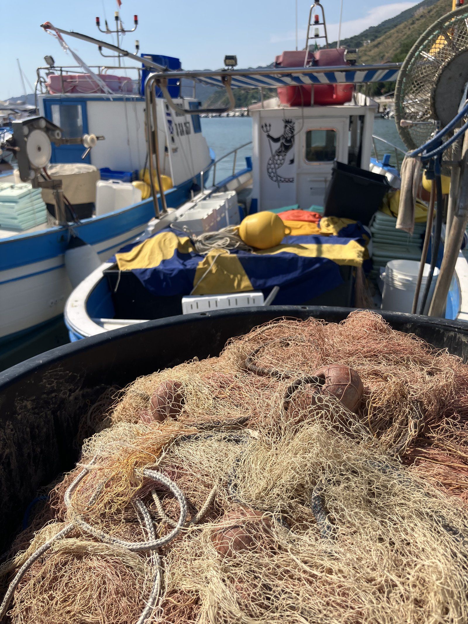 Menaica fishing nets in the foreground with blue and white boats in the harbour of Pisciotta.