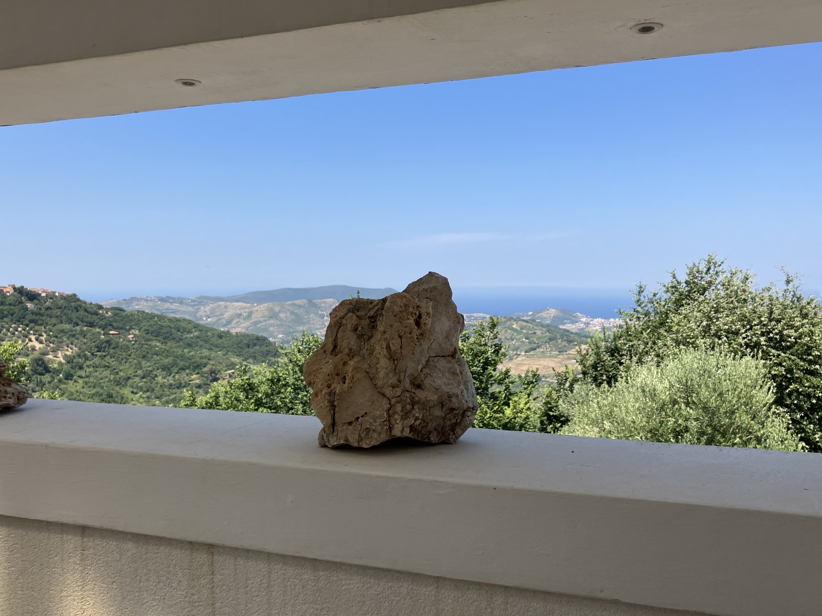 A stone resting on a white parapet at Santomiele, the Cilento hills and sea in the distance.