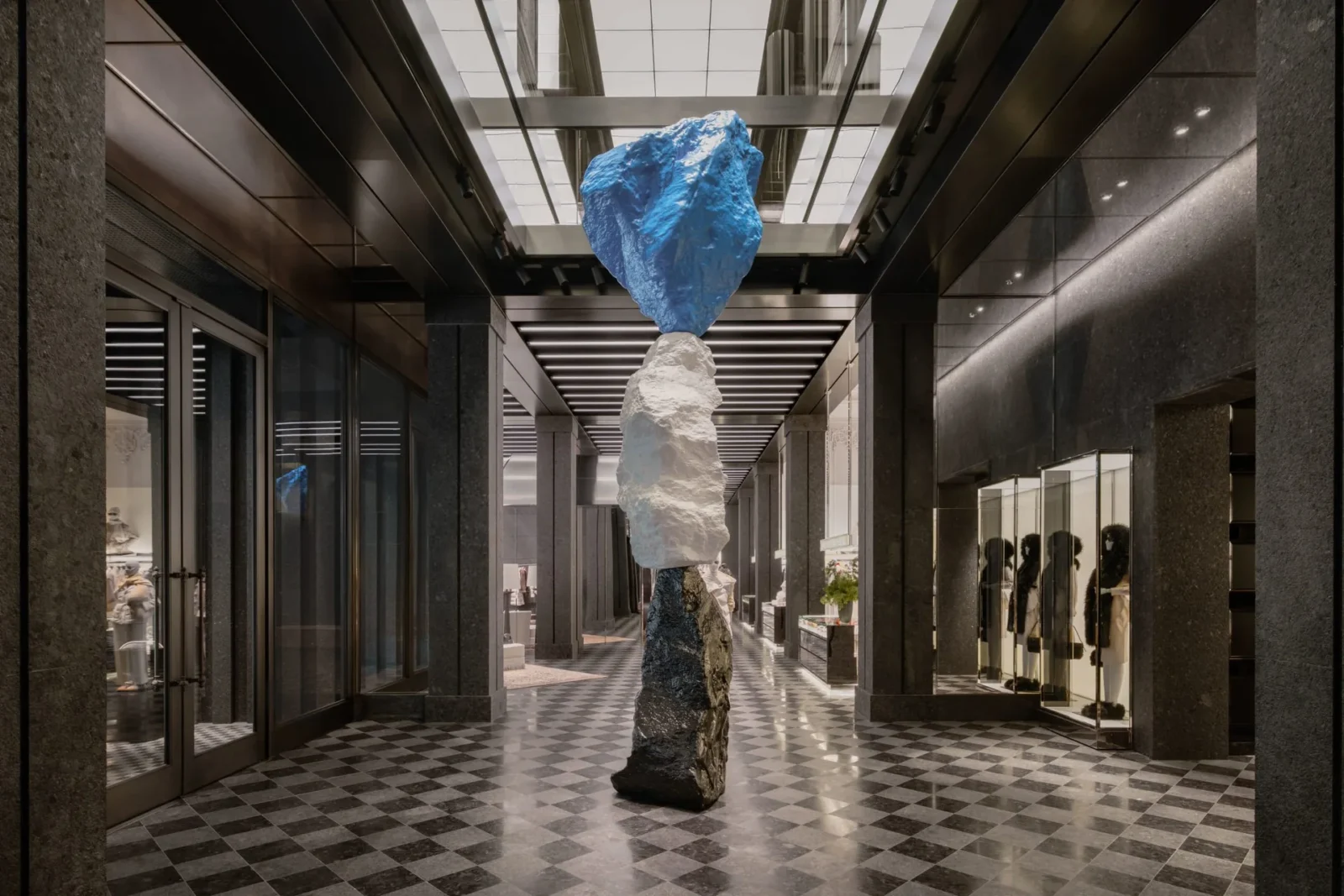 Stacked stone sculpture by Ugo Rondinone rising from a checkerboard floor inside Moncler Fifth Avenue, the largest Moncler store, at 767 Fifth Avenue in New York.