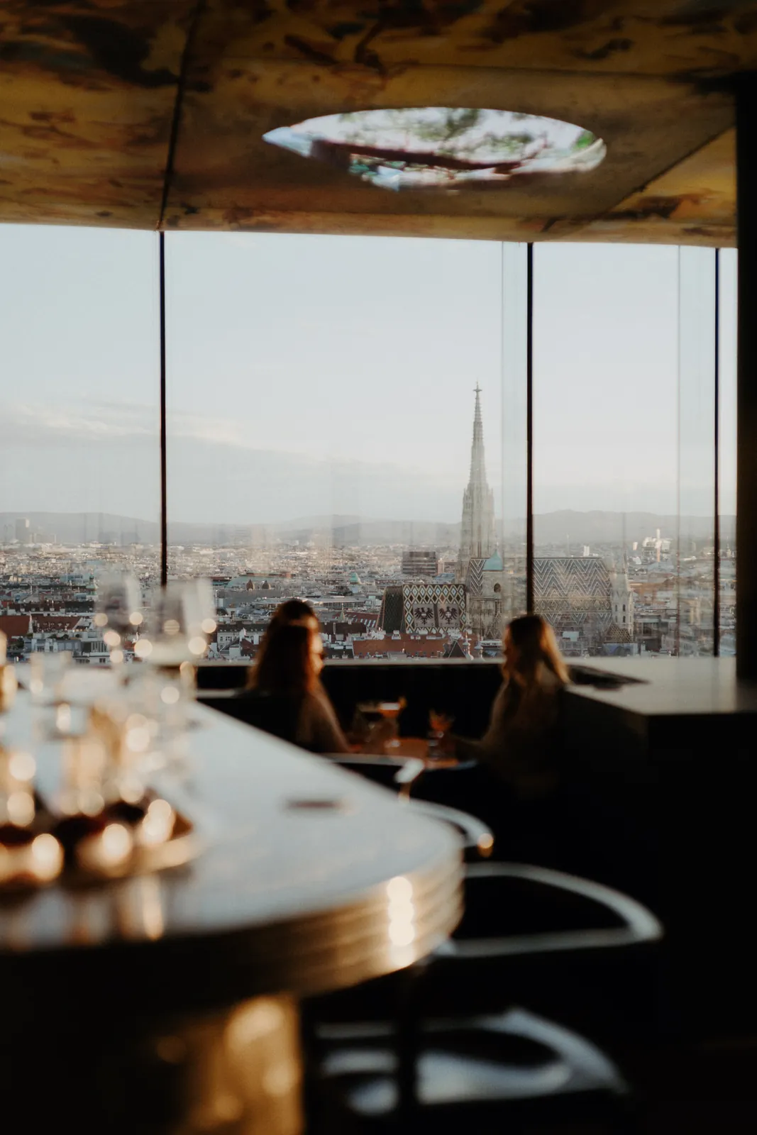 Two guests in conversation at a window table of Das LOFT, St Stephen's Cathedral beyond the glass.