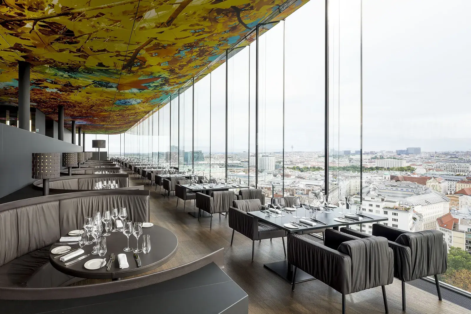 A round banquette behind the window tables of Das LOFT, Vienna below the glass façade.