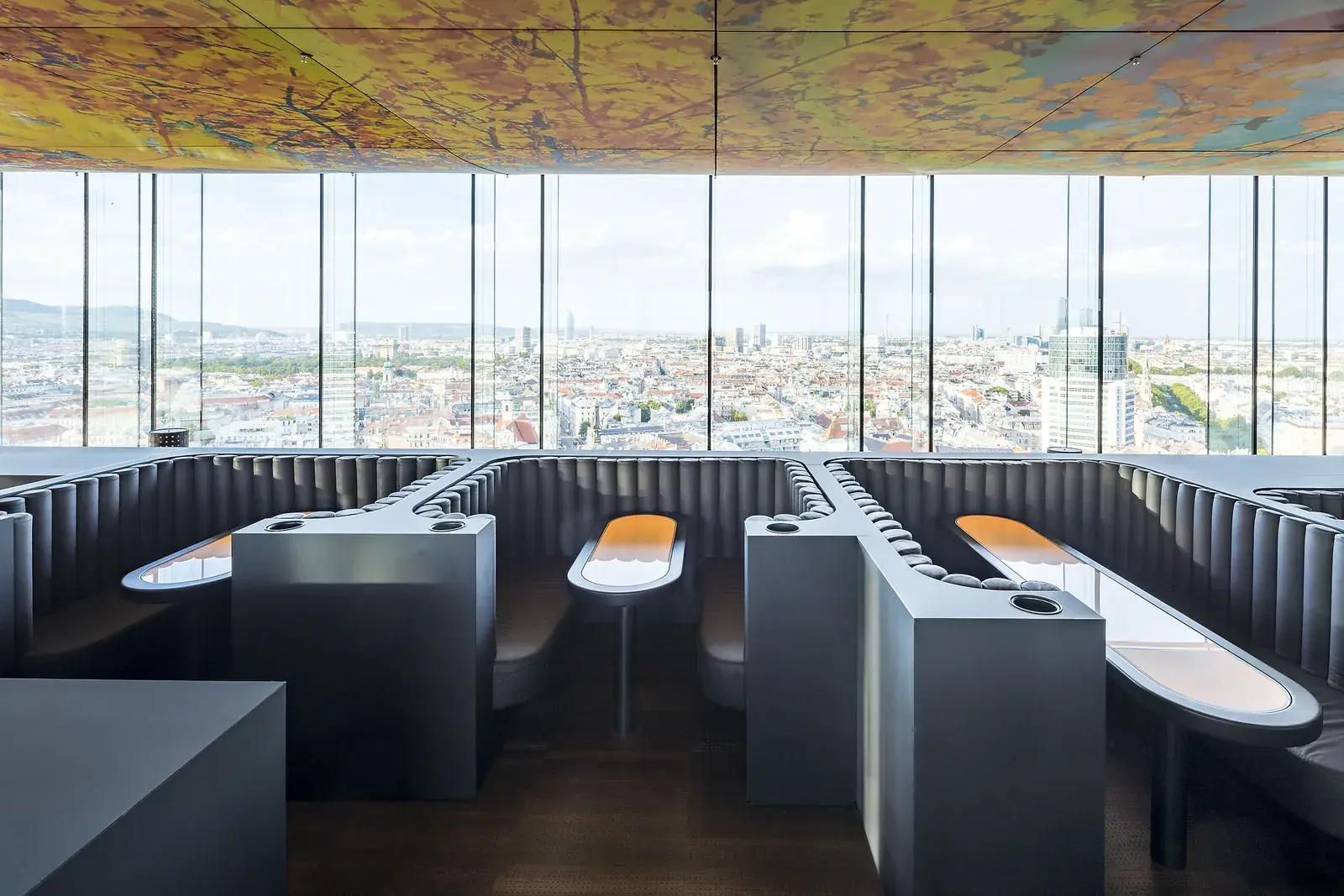 Dark booths with lit tables at Das LOFT, all facing the glass and the city.