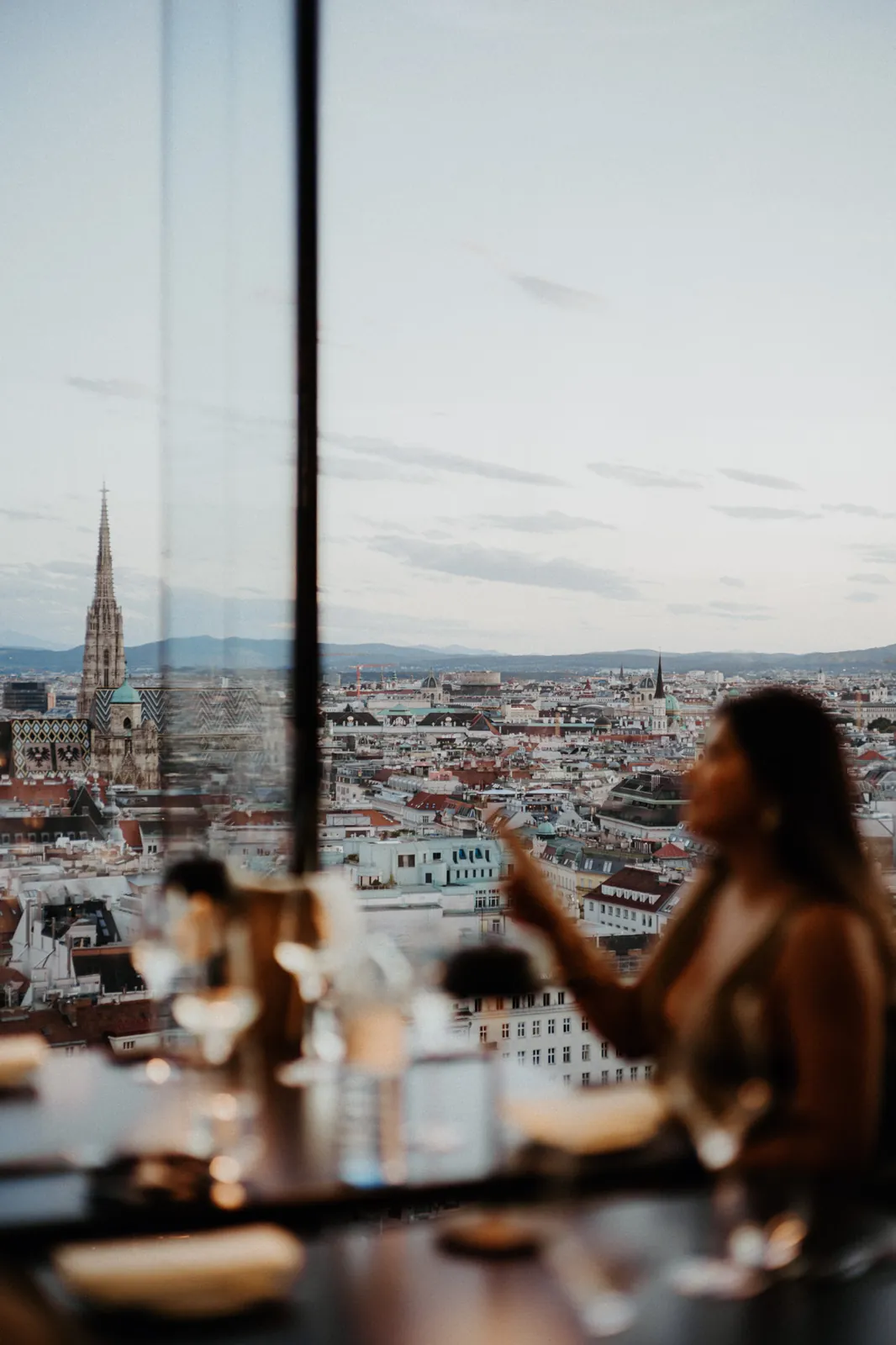 A guest at a window table of Das LOFT in the evening, St Stephen's Cathedral and the roofs of Vienna beyond.