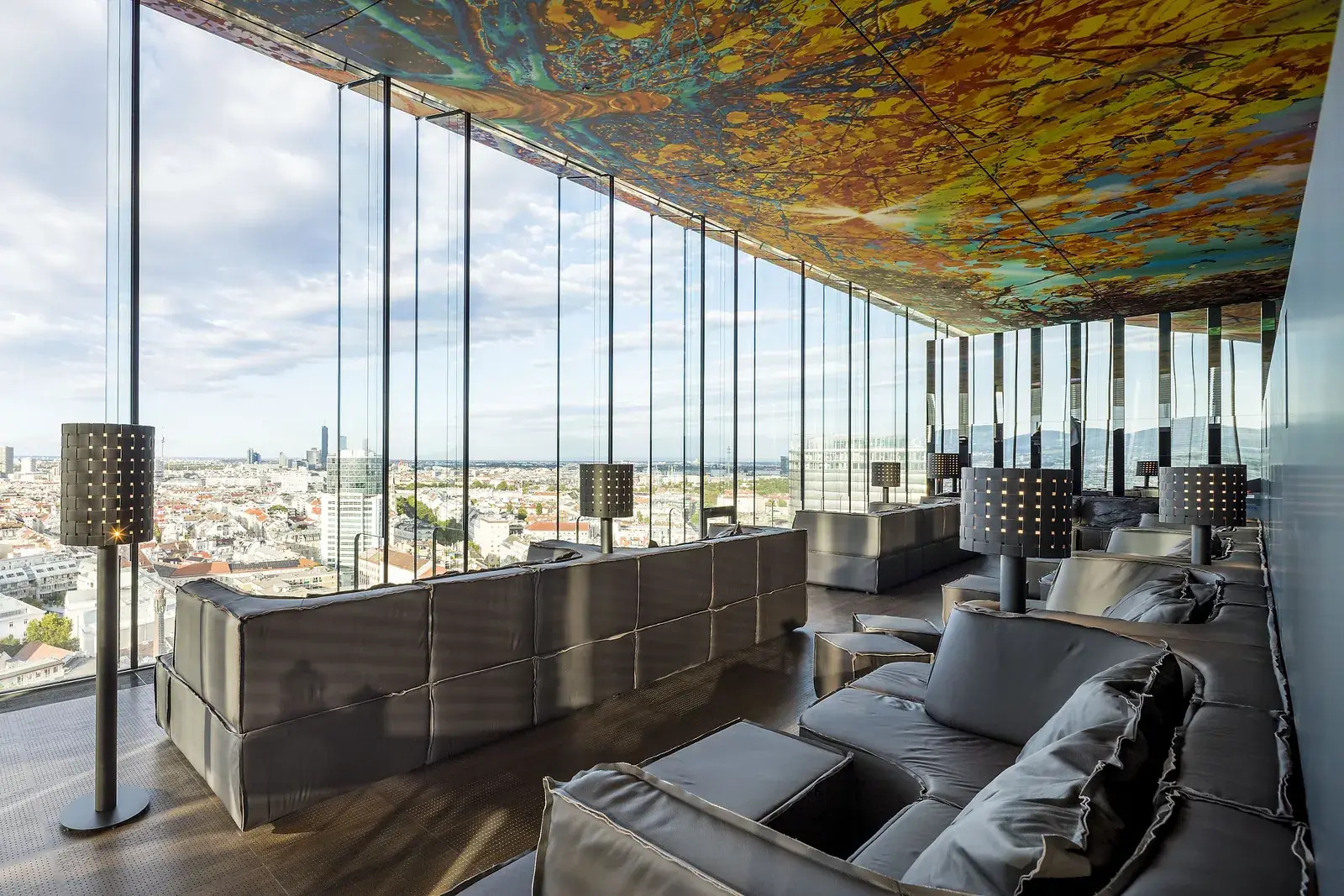 Deep leather sofas and perforated floor lamps in the lounge of Das LOFT along the glass façade.