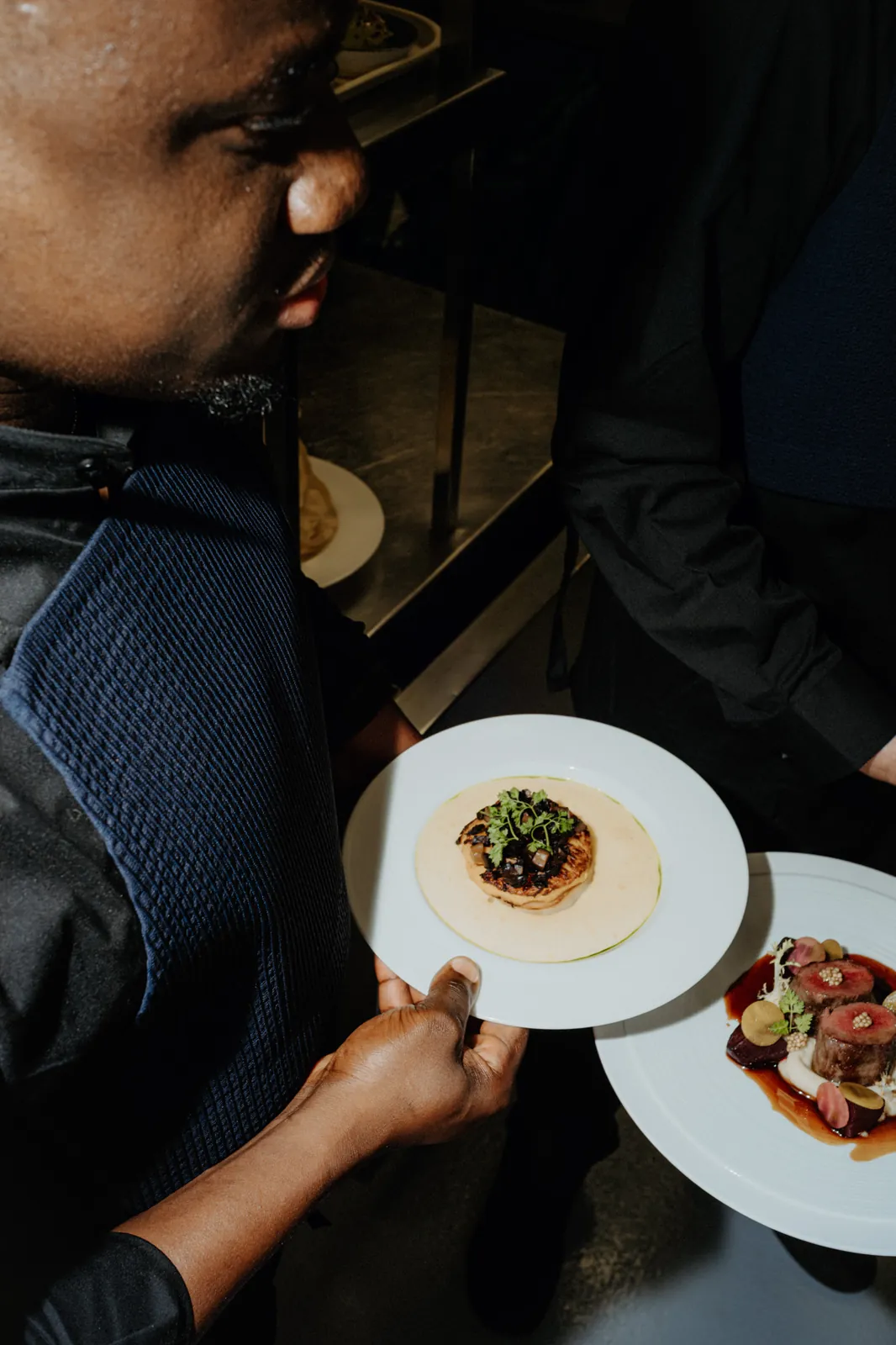 A waiter's hands carrying plates through the dark dining room of Das LOFT.