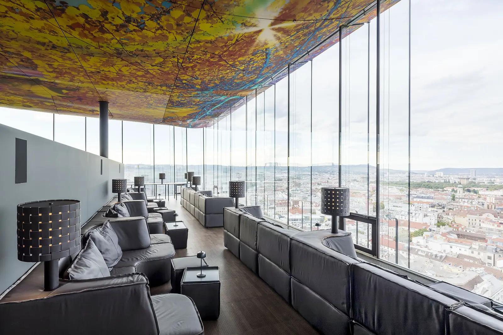 Leather sofas and perforated floor lamps in the lounge of Das LOFT beneath Pipilotti Rist's ceiling, Vienna beyond the glass.