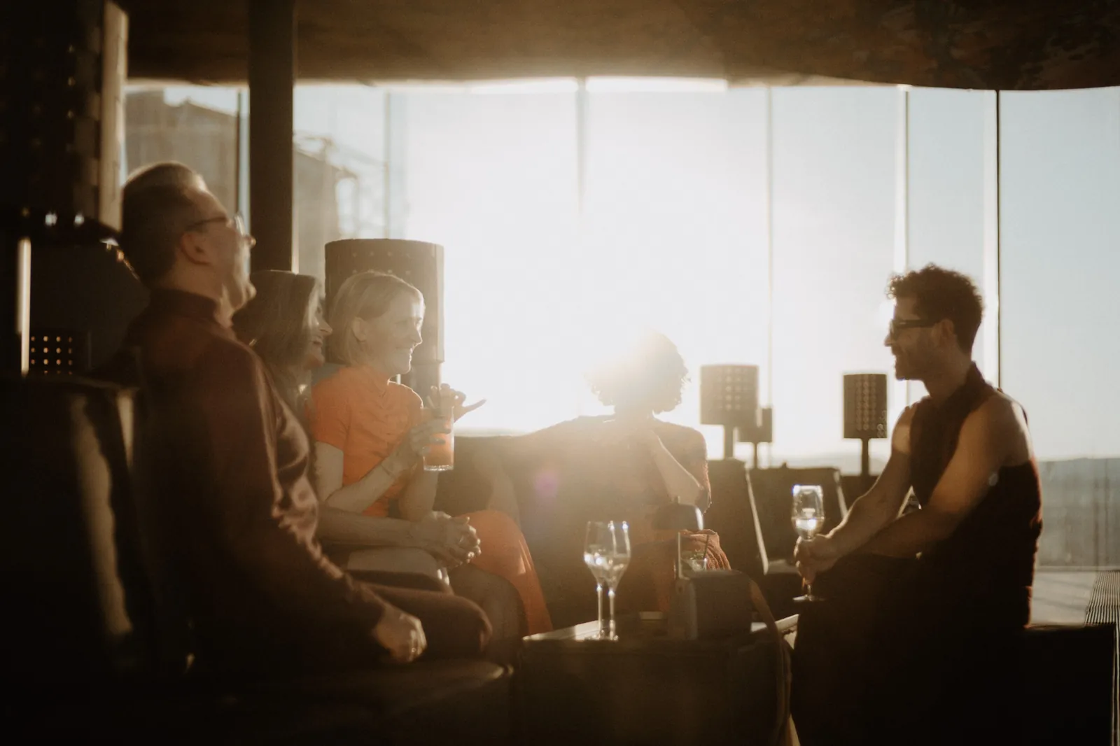 Guests talking on the lounge sofas of Das LOFT, backlit by the setting sun.