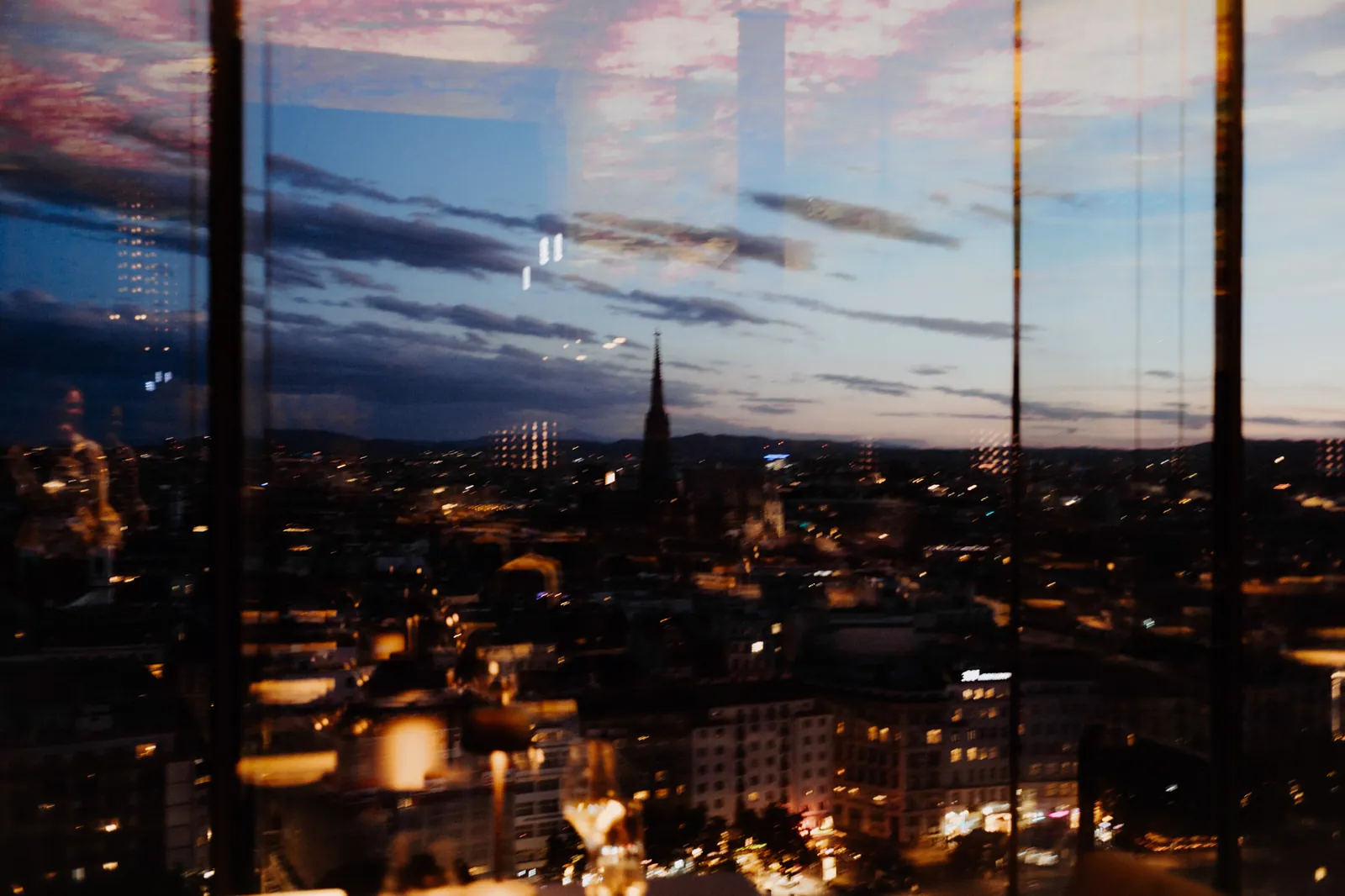 Vienna at blue hour through the glass façade of Das LOFT, St Stephen's Cathedral on the skyline.