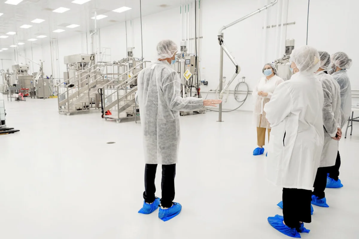 Visitors in protective clothing in a Capsum production hall with mixing vessels and steel platforms.