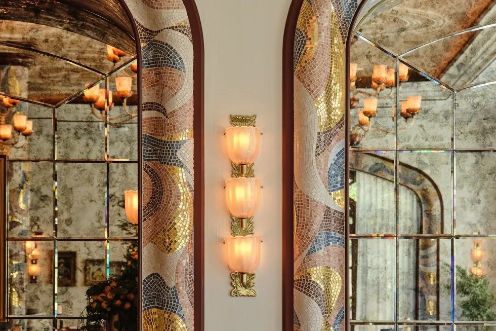 A sconce of three ribbed glass cups on a brass stem between two mosaic arches at Carbone Riviera in Las Vegas.