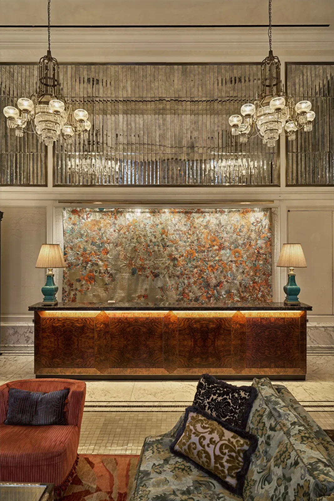 Two glass chandeliers above a marquetry reception desk at The Fifth Avenue Hotel in New York.