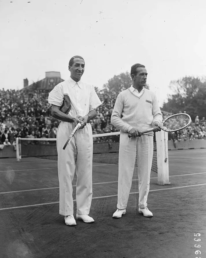 René Lacoste in his short-sleeved piqué shirt beside Henri Cochet in a long-sleeved sweater, on court at Roland Garros in 1928.