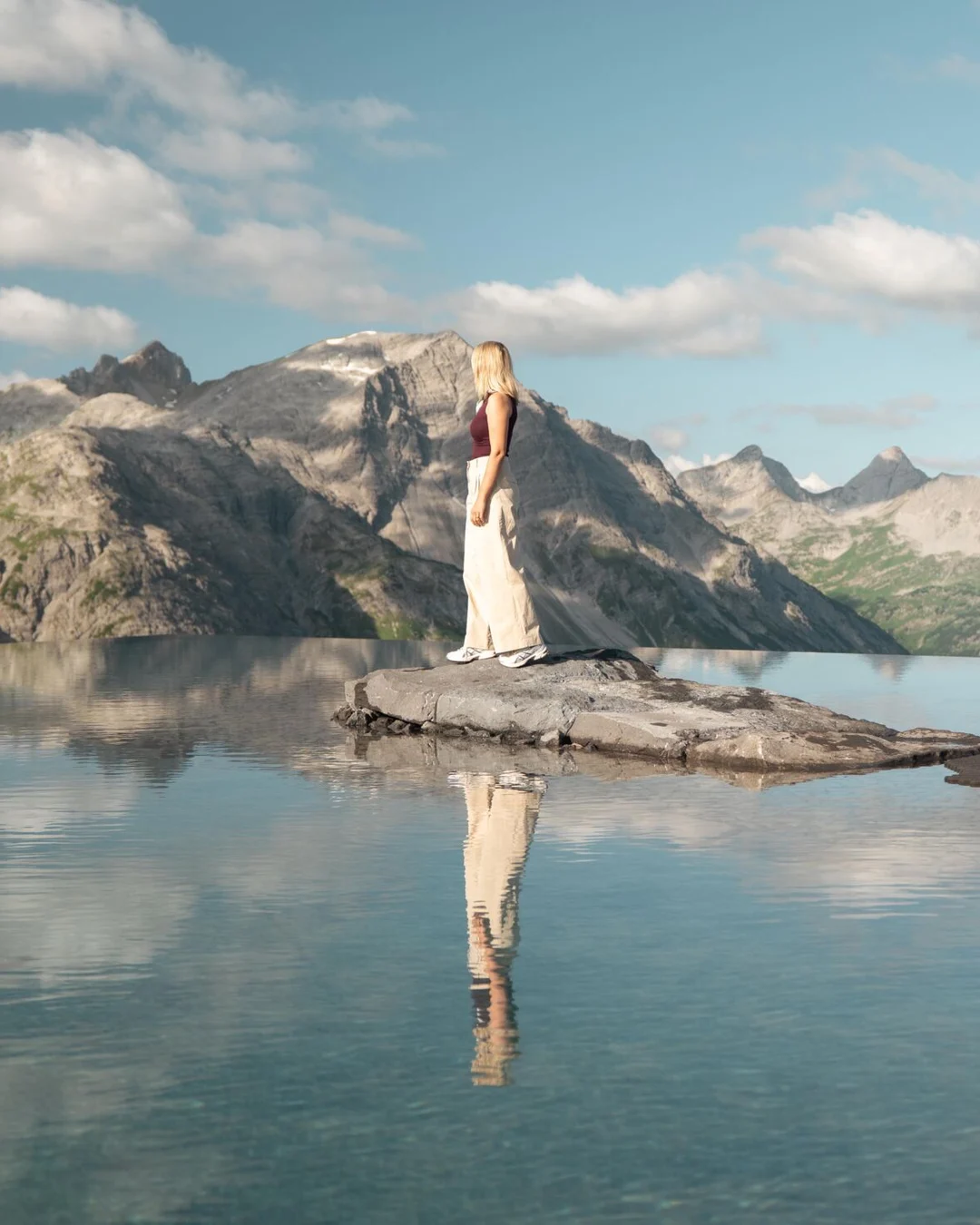A visitor stands on the rock in the middle of the Lech Mountain Mirror