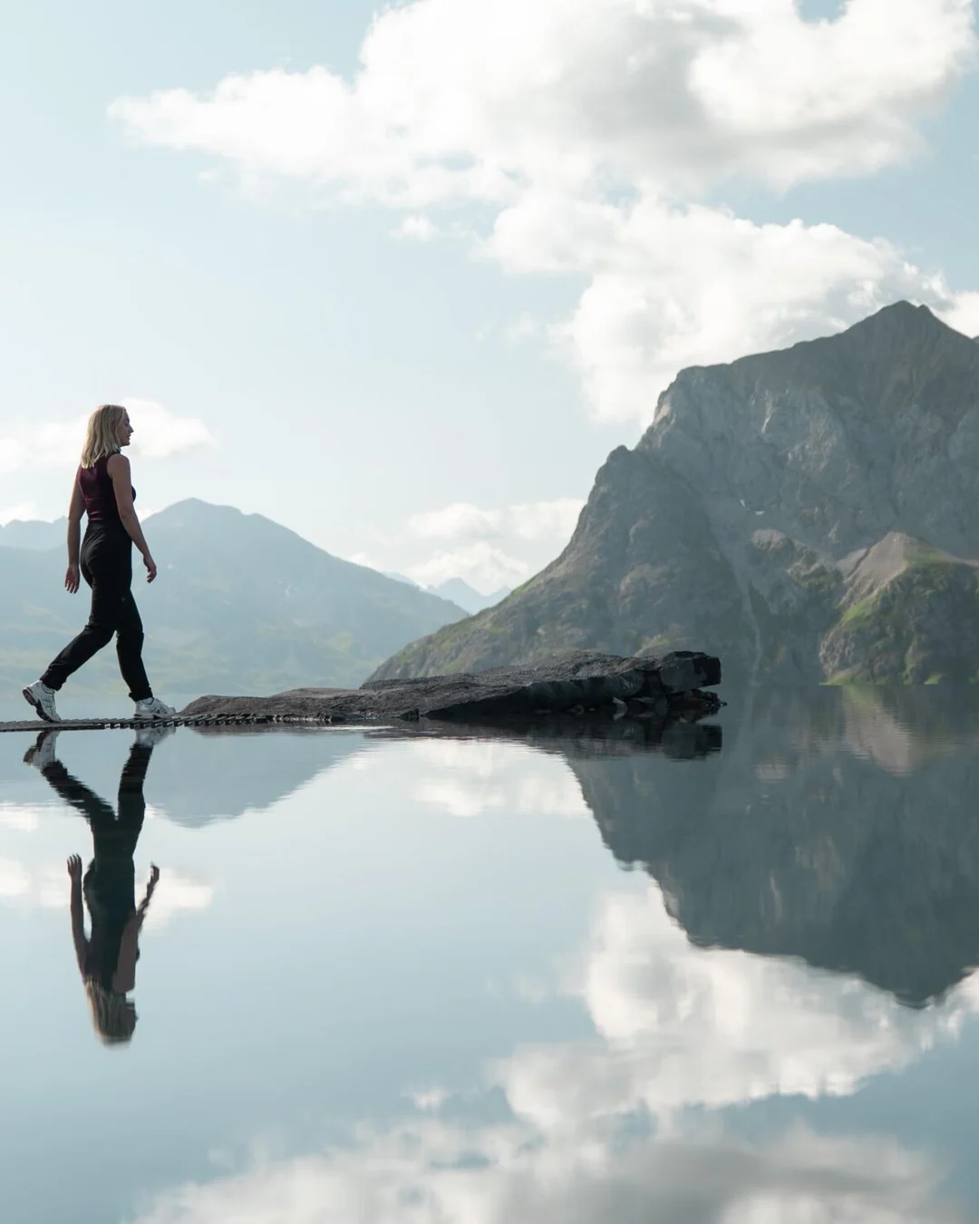 A visitor crosses the stepping stones of the Lech Mountain Mirror, reflected in the water