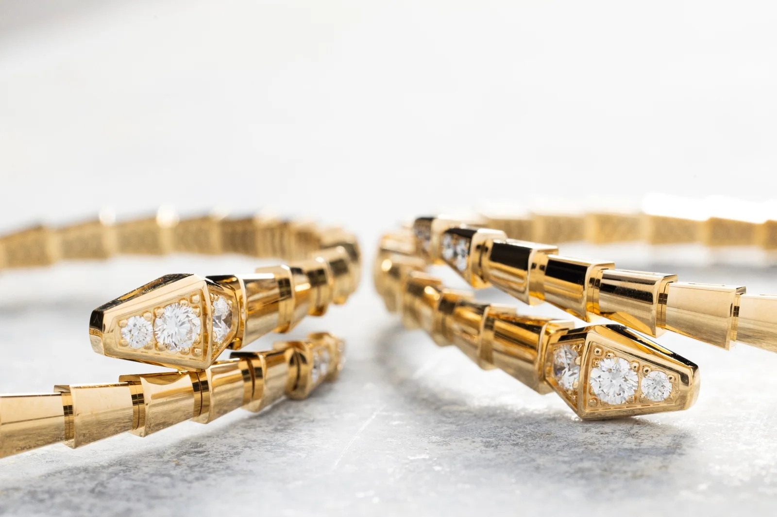Two gold Bvlgari Serpenti bracelets set with diamonds, lying on a pale stone surface