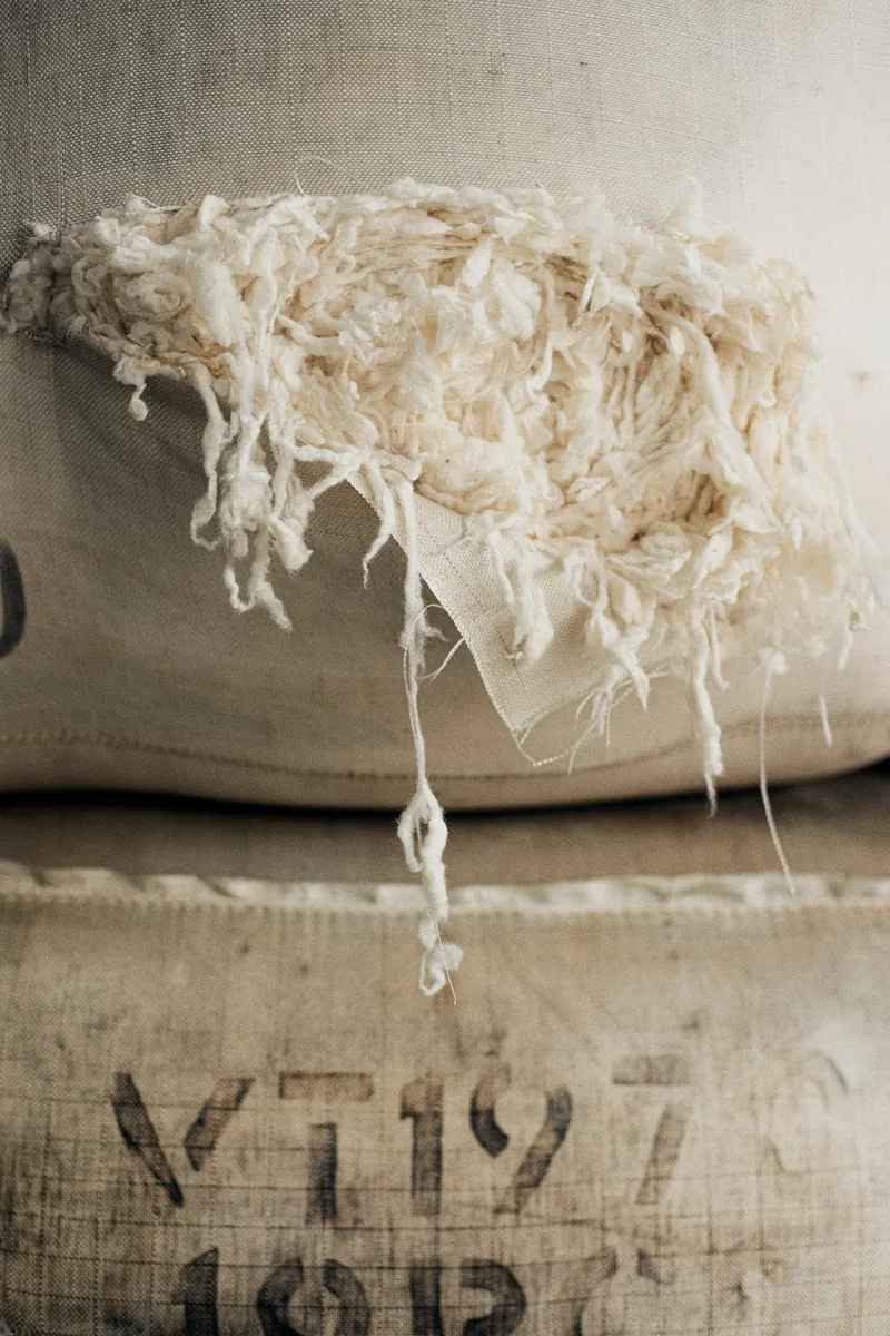 Loose wool fibre spilling over stacked jute sacks with stencilled numbers, the raw material Prato's textile district recycles into new carded wool.