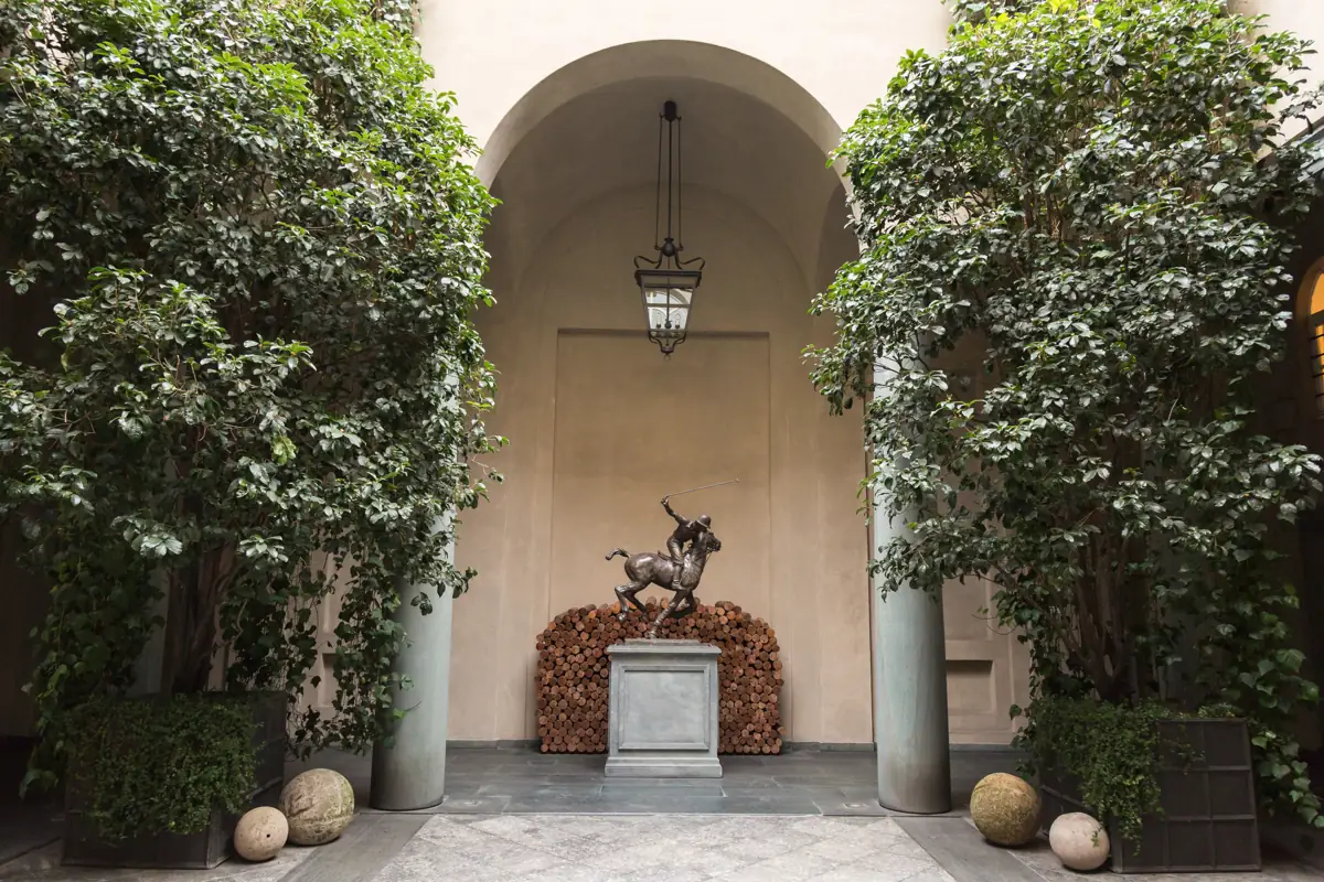 The courtyard of the Ralph Lauren Palazzo in Milan with a bronze polo player sculpture between climbing plants.