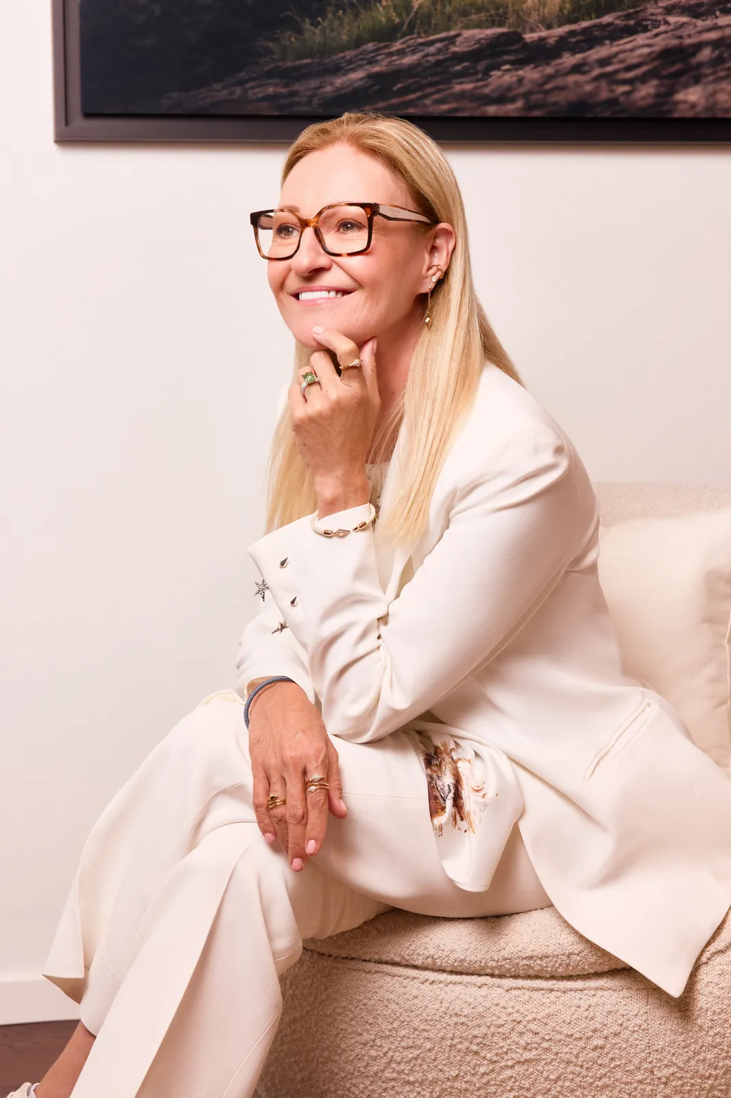 Sandrine Thibaud, founder of Fullord Geneva, in a cream suit, seated and smiling with her chin resting on her hand.