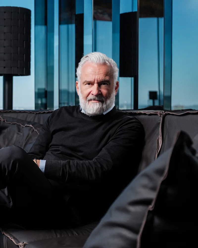 Stephan Ferenczy, co-founder of BEHF Architects, in black on a leather sofa in the lounge of Das LOFT, Vienna behind the glass.