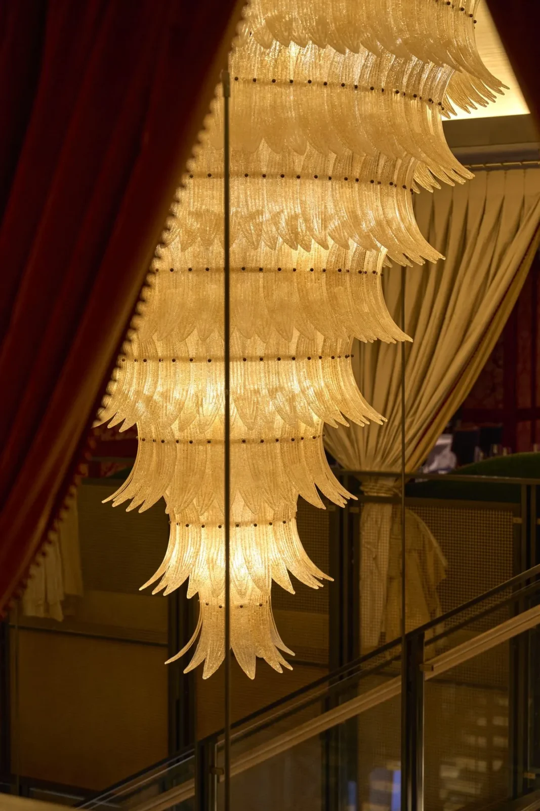 A tall chandelier of hand-formed glass leaves glowing between red velvet curtains at ZZ’s Club in New York.