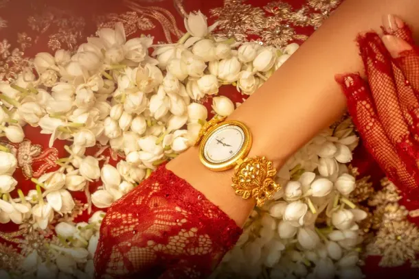 An 18-carat gold Nebula watch by Titan and Tarun Tahiliani on a bride's wrist, resting on jasmine flowers and red lace. Photo: Courtesy of Titan Company