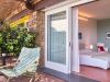 Junior Suite at Borgo La Pietraia, private terrace with green garden chair opening to light-filled room with local sandstone wall, yellow window accent and contemporary art, Cilento