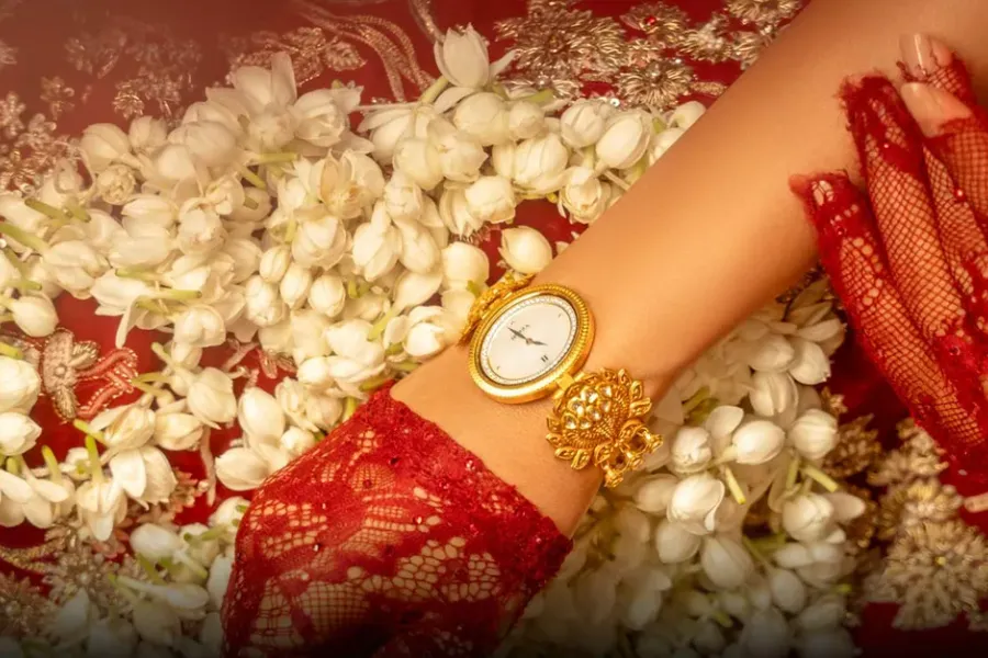 An 18-carat gold Nebula watch by Titan and Tarun Tahiliani on a bride's wrist, resting on jasmine flowers and red lace. Photo: Courtesy of Titan Company