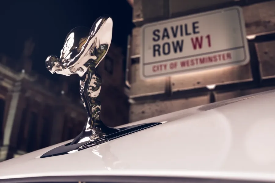 The bonnet figure of the one-of-one Ghost Savile Row in front of the street that gave the word bespoke its meaning. Bespoke designer Ieuan Hatherall built the car outward from an embroidery of 250,000 stitches beneath the rear armrest. Rolls-Royce Motor Cars | In Courtesy of Rolls-Royce