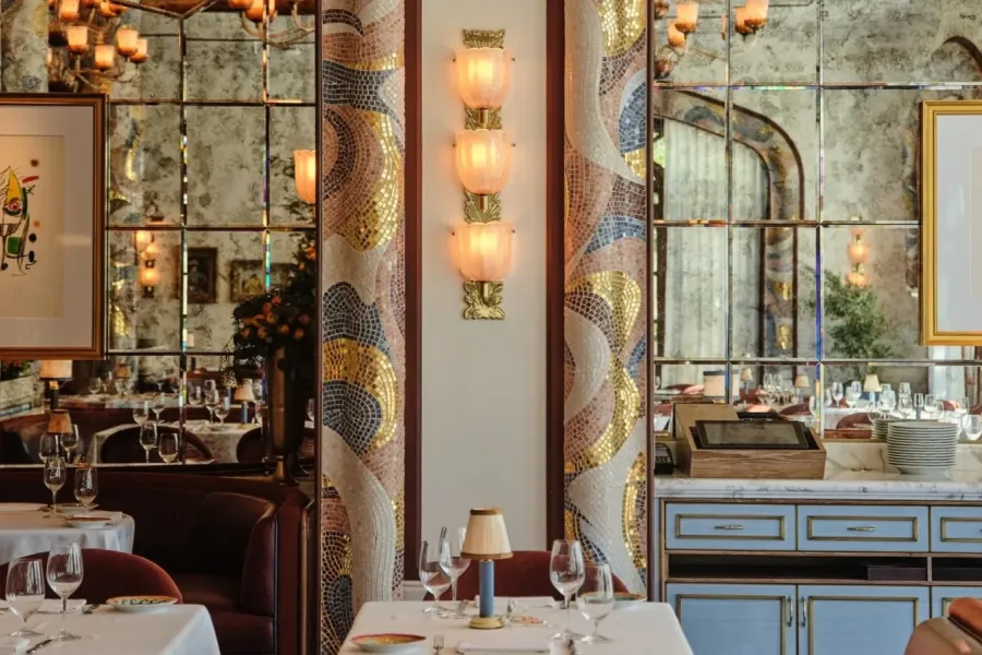 The dining room of Carbone Riviera at the Bellagio in Las Vegas, with mosaic arches, a sconce of three ribbed glass cups on a brass stem and tables laid in white. | Credit: Courtesy of Sogni di Cristallo