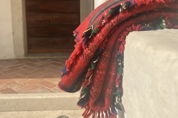 A red checked wool blanket with tufted, fringed edges lies folded over a stone wall in the courtyard of Lanificio Bottoli in Vittorio Veneto.