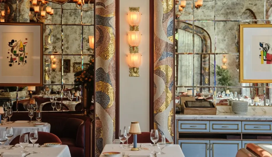 The dining room of Carbone Riviera at the Bellagio in Las Vegas, with mosaic arches, a sconce of three ribbed glass cups on a brass stem and tables laid in white. | Credit: Courtesy of Sogni di Cristallo