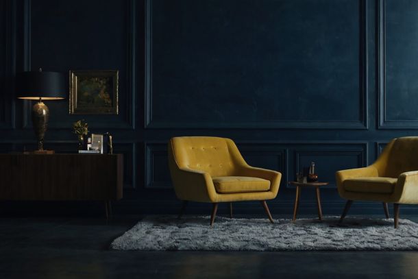 The Architecture of Stillness: Two iconic yellow armchairs set against a deep monolithic wall, translating the philosophical core of Silent Luxury and Well Living into spatial gravity.