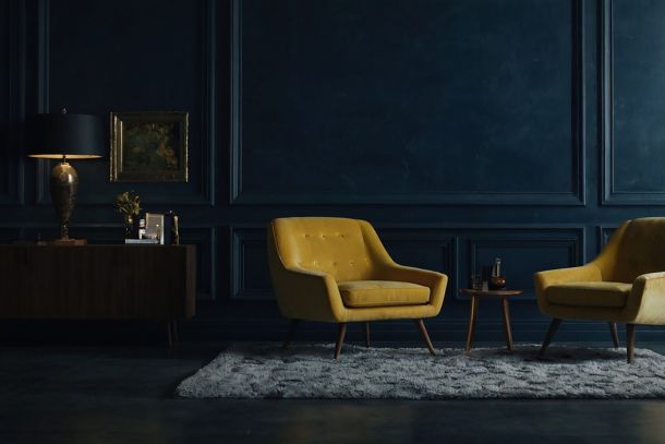 The Architecture of Stillness: Two iconic yellow armchairs set against a deep monolithic wall, translating the philosophical core of Silent Luxury and Well Living into spatial gravity.